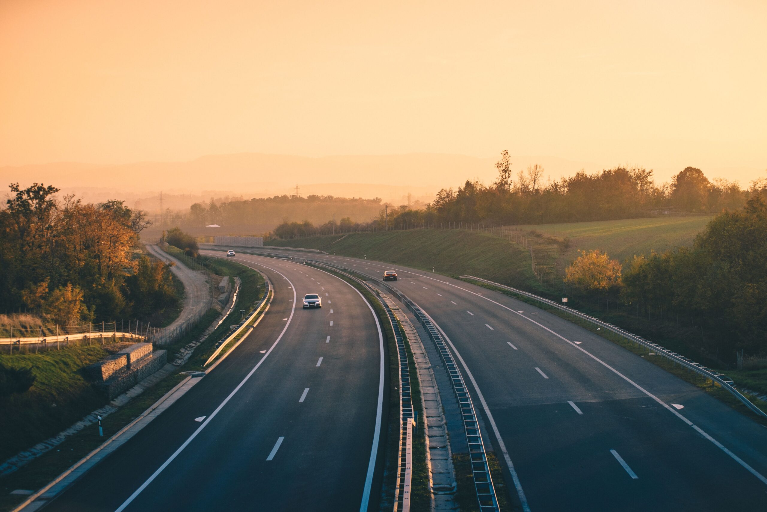 Aerial view of an empty highway with two cars, surrounded by trees and hills, illustrating the open road for cross-country travel in 2025.
