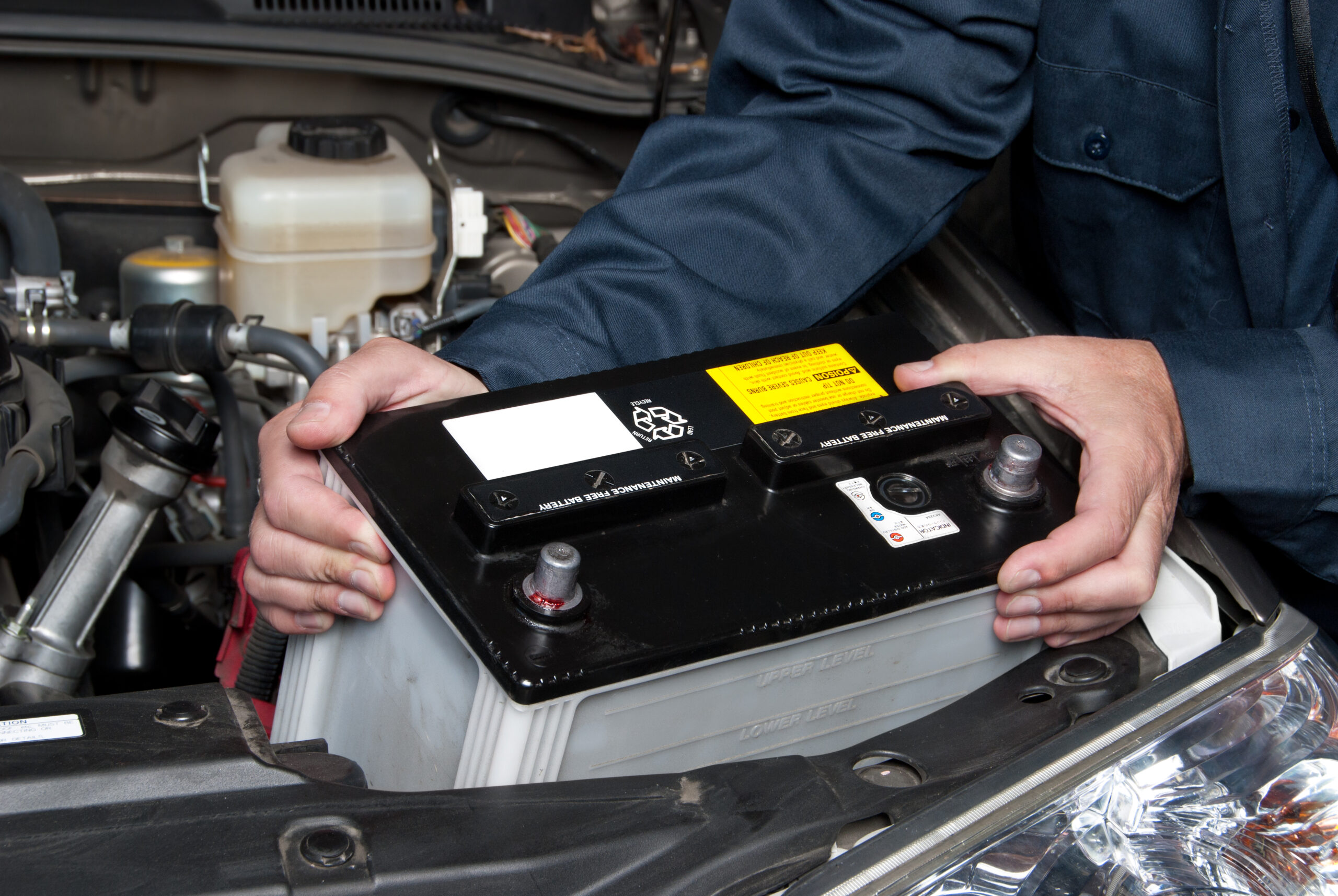Auto mechanic replacing car battery under the hood, emphasizing vehicle maintenance for summer heat and battery care.