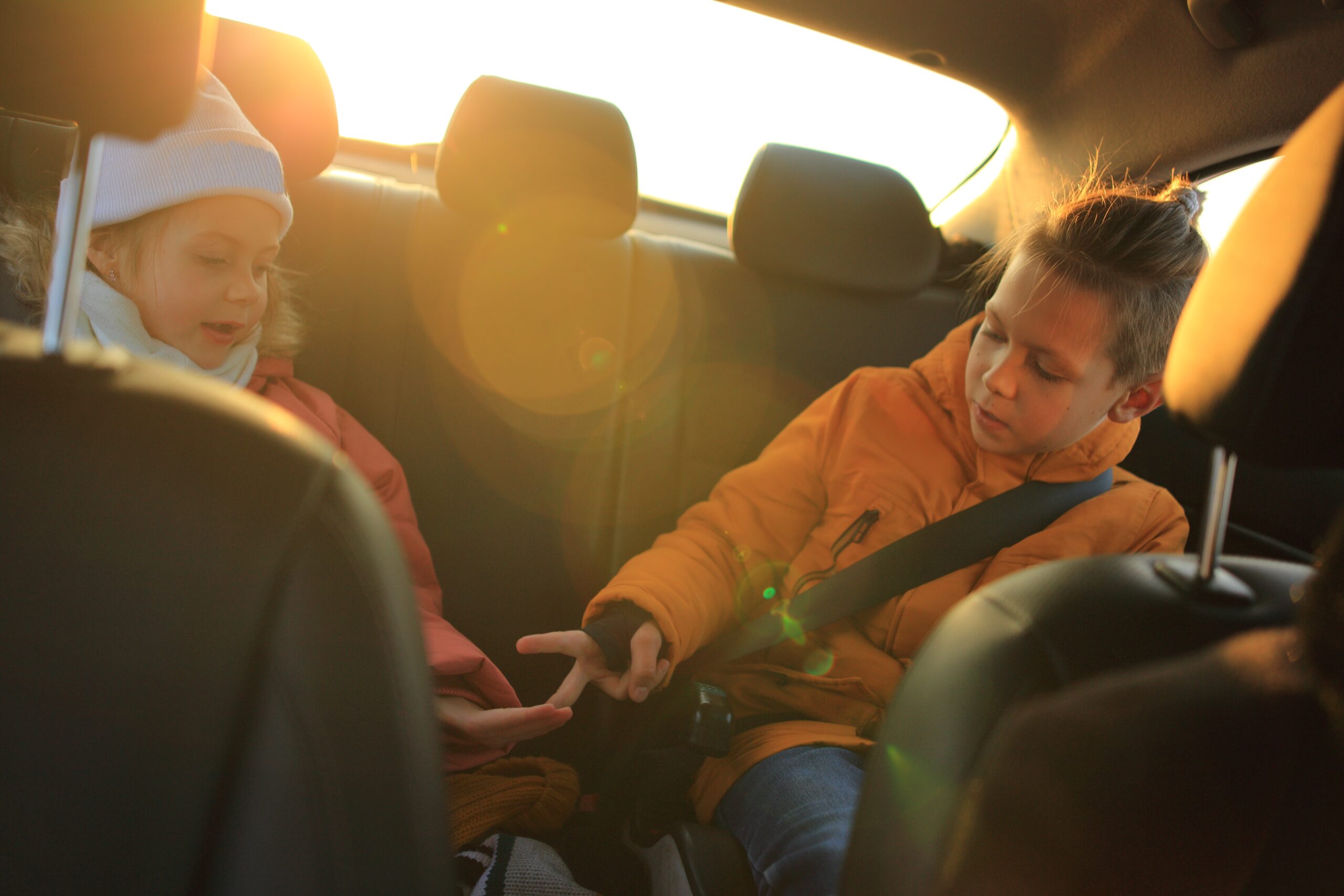 Children seated in the back seat of a car, engaged in a game, with sunlight streaming through the window, emphasizing the importance of safety during back-to-school driving.