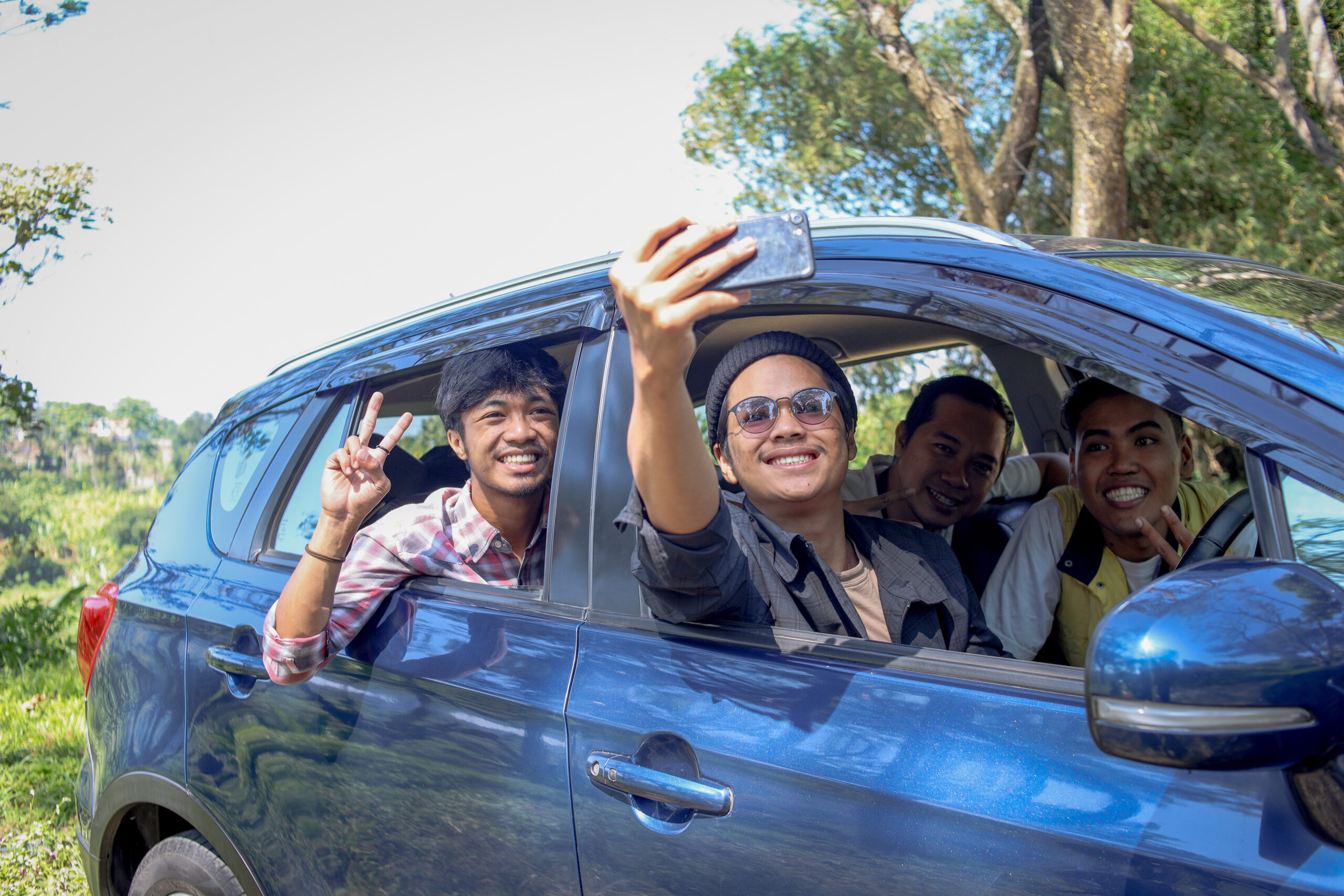 Friends taking a selfie in a car during a road trip, highlighting camaraderie and adventure, relevant to college students seeking insurance for older vehicles.
