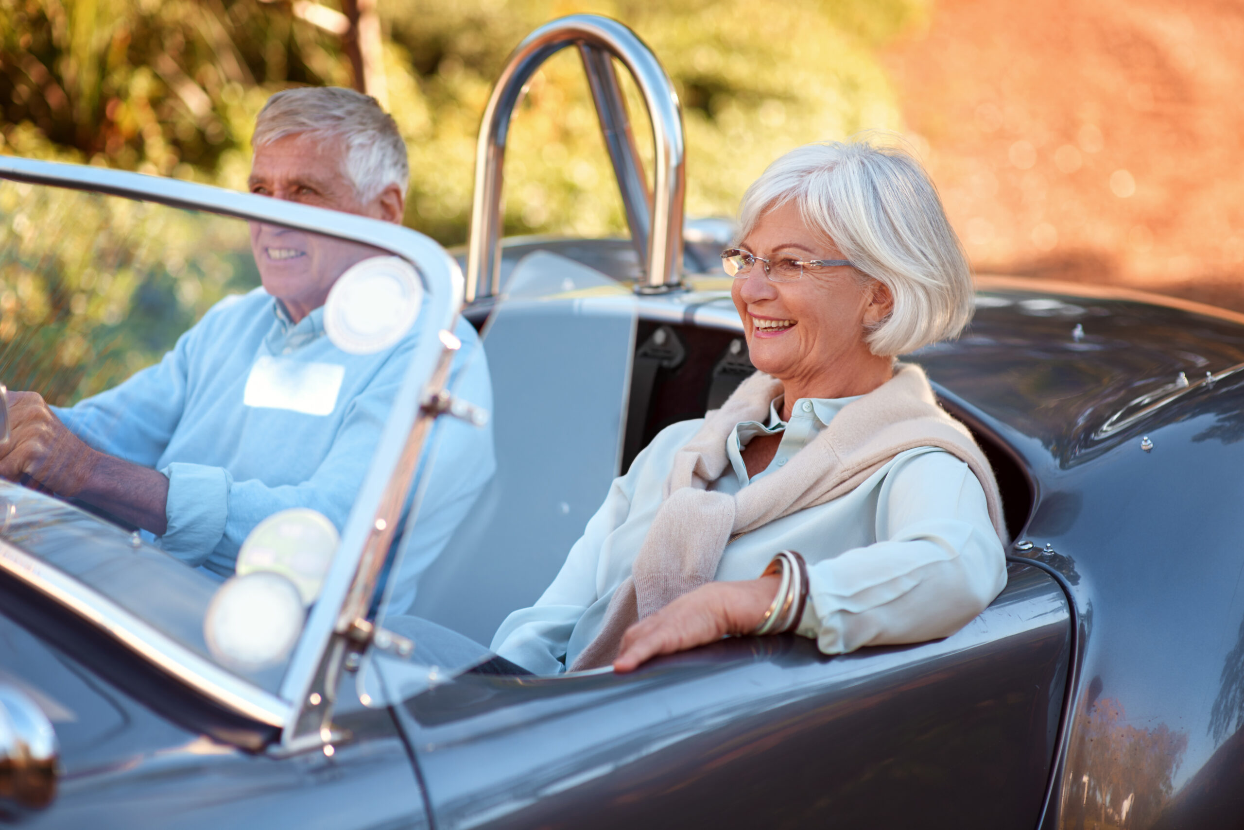 Senior couple enjoying a drive in a convertible car, smiling and relaxed, highlighting the importance of comfort and confidence for older drivers.