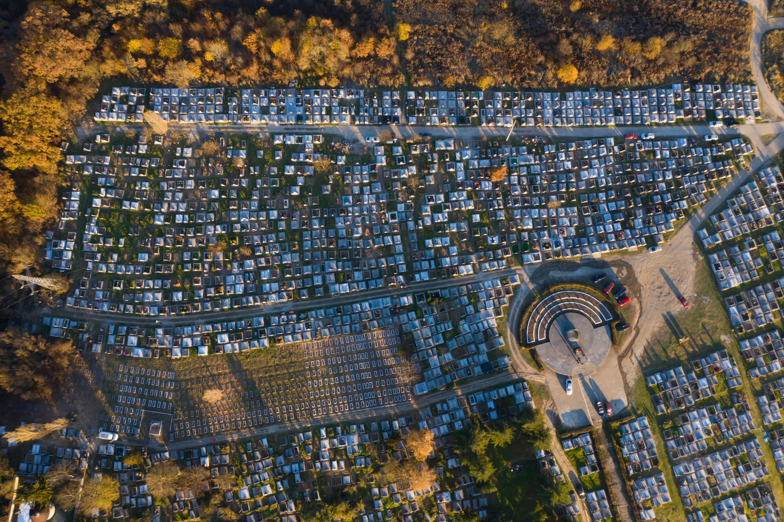 Aerial view of a cemetery with rows of marble graves surrounded by autumn foliage, emphasizing the serene and reflective atmosphere.