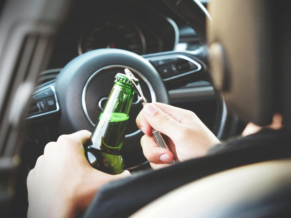Person opening a green beer bottle inside a car, highlighting risks of drinking and driving during holiday celebrations.