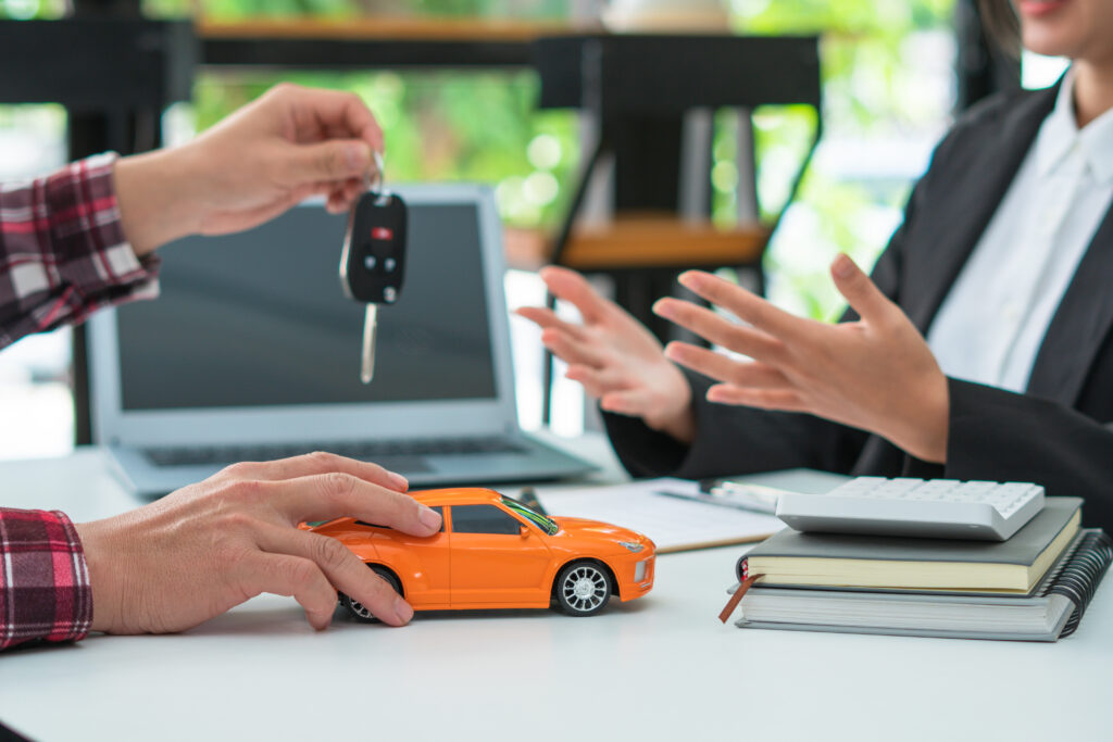 Person handing over car keys to a rental agent, with a toy car on the table, illustrating car rental process and insurance considerations.