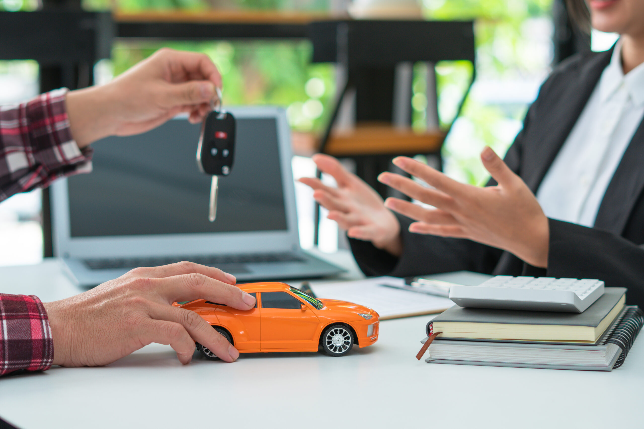Person handing over car keys to a rental agent, with a toy car on the table, symbolizing car insurance discussions and updates.