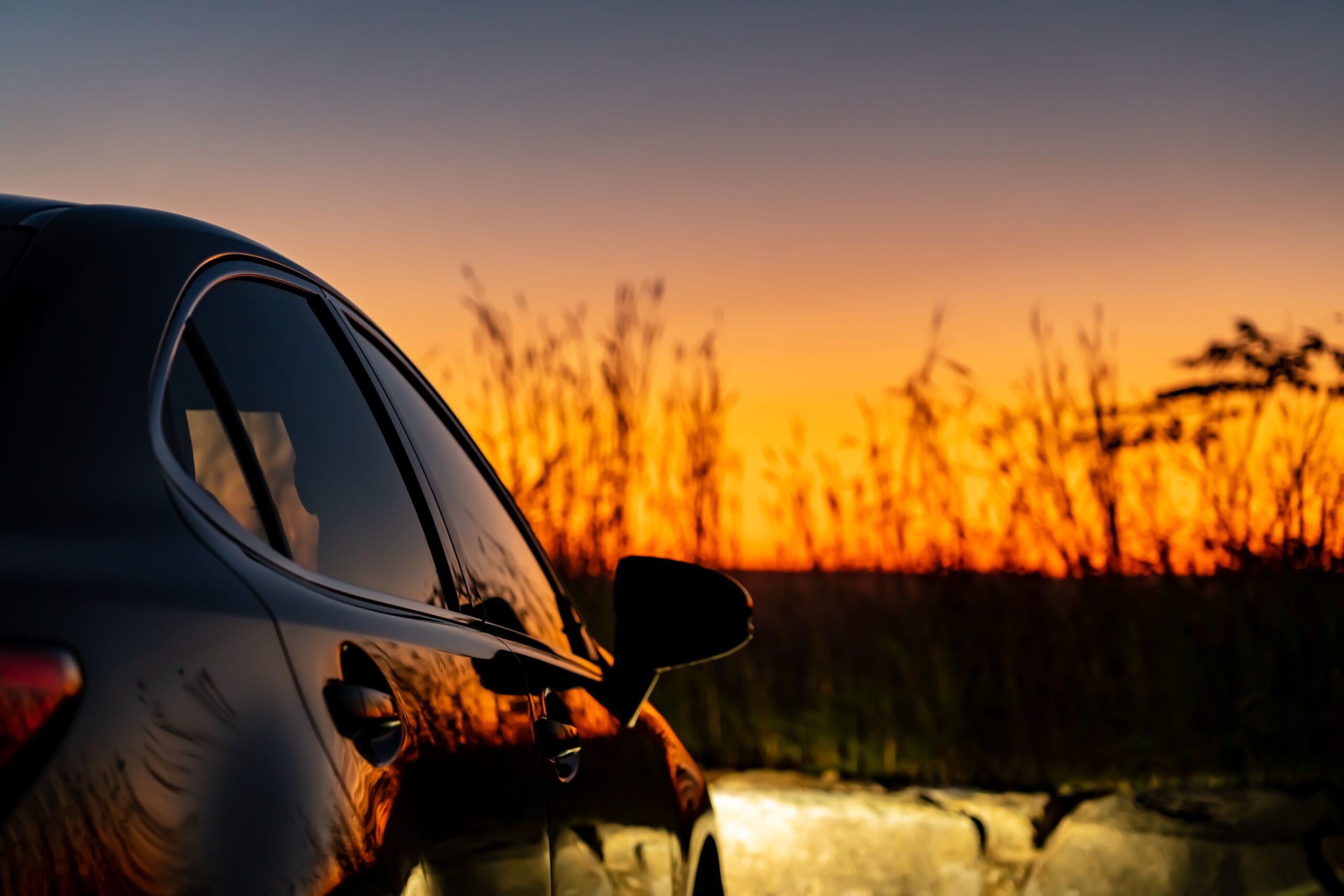Shiny black car parked against a vibrant sunset, symbolizing driving safety during darker evening commutes.