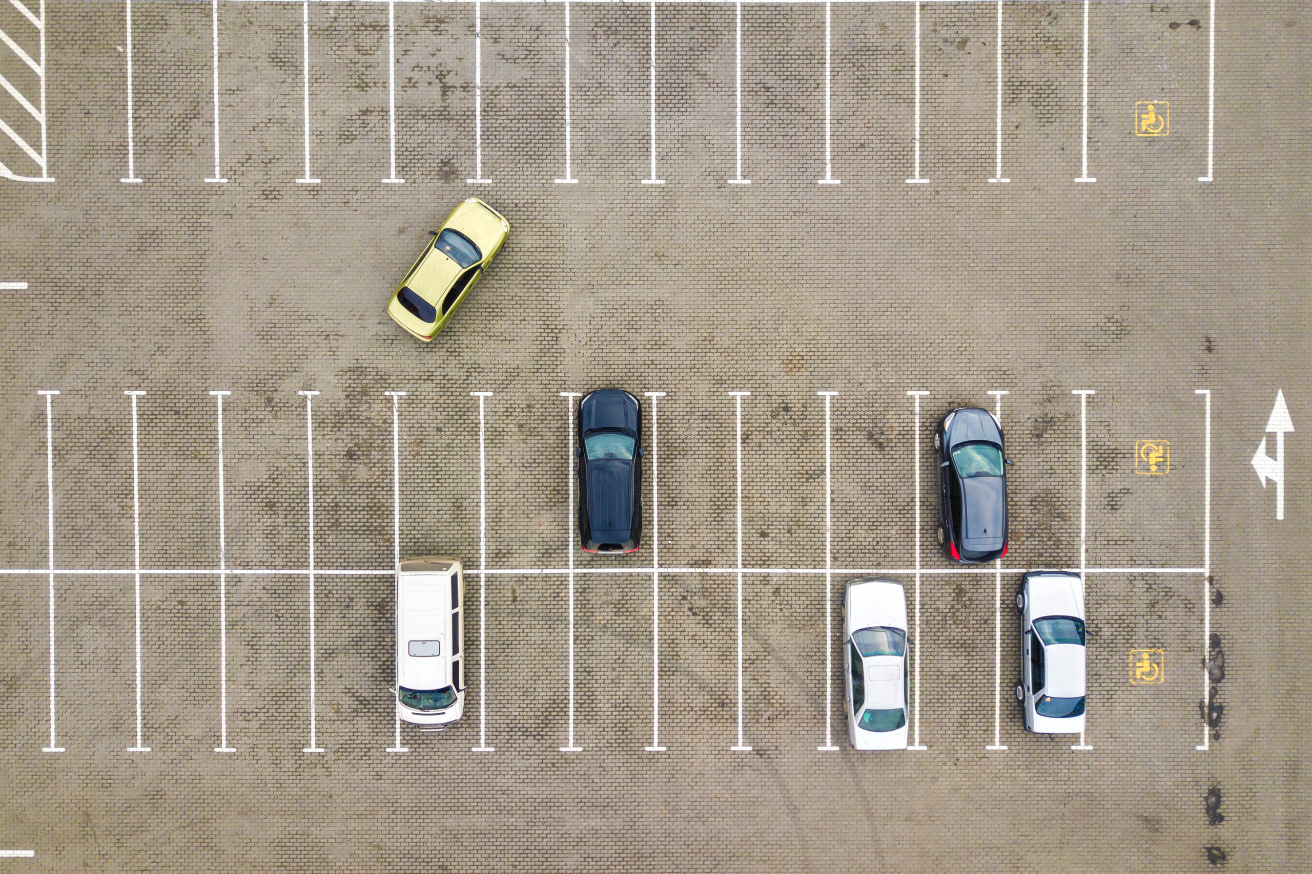 Aerial view of a nearly empty parking lot with several parked cars, highlighting the importance of early rental car bookings during Black Friday travel.