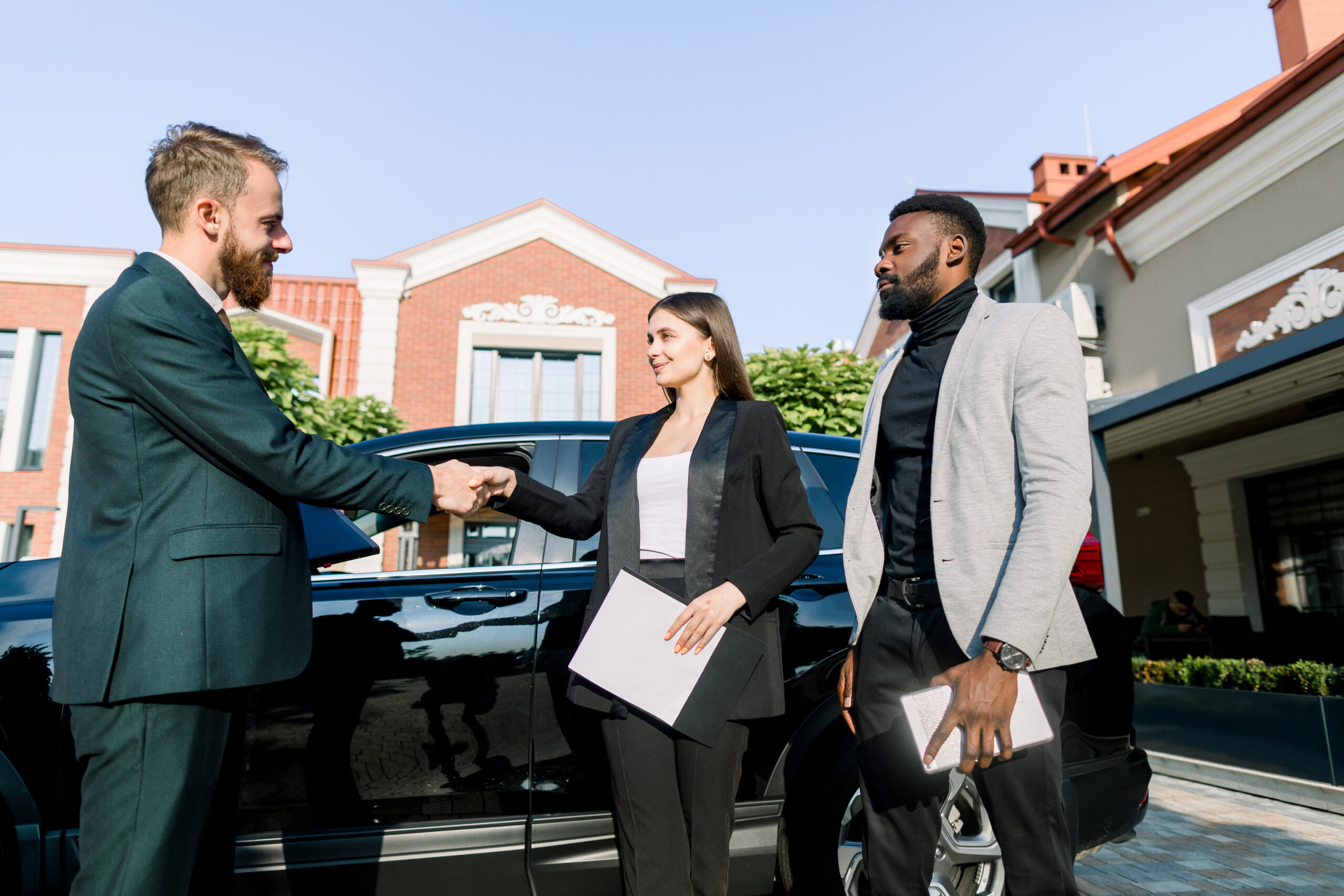 Business professionals shaking hands near a car, discussing insurance options before travel, emphasizing preparation and coverage.