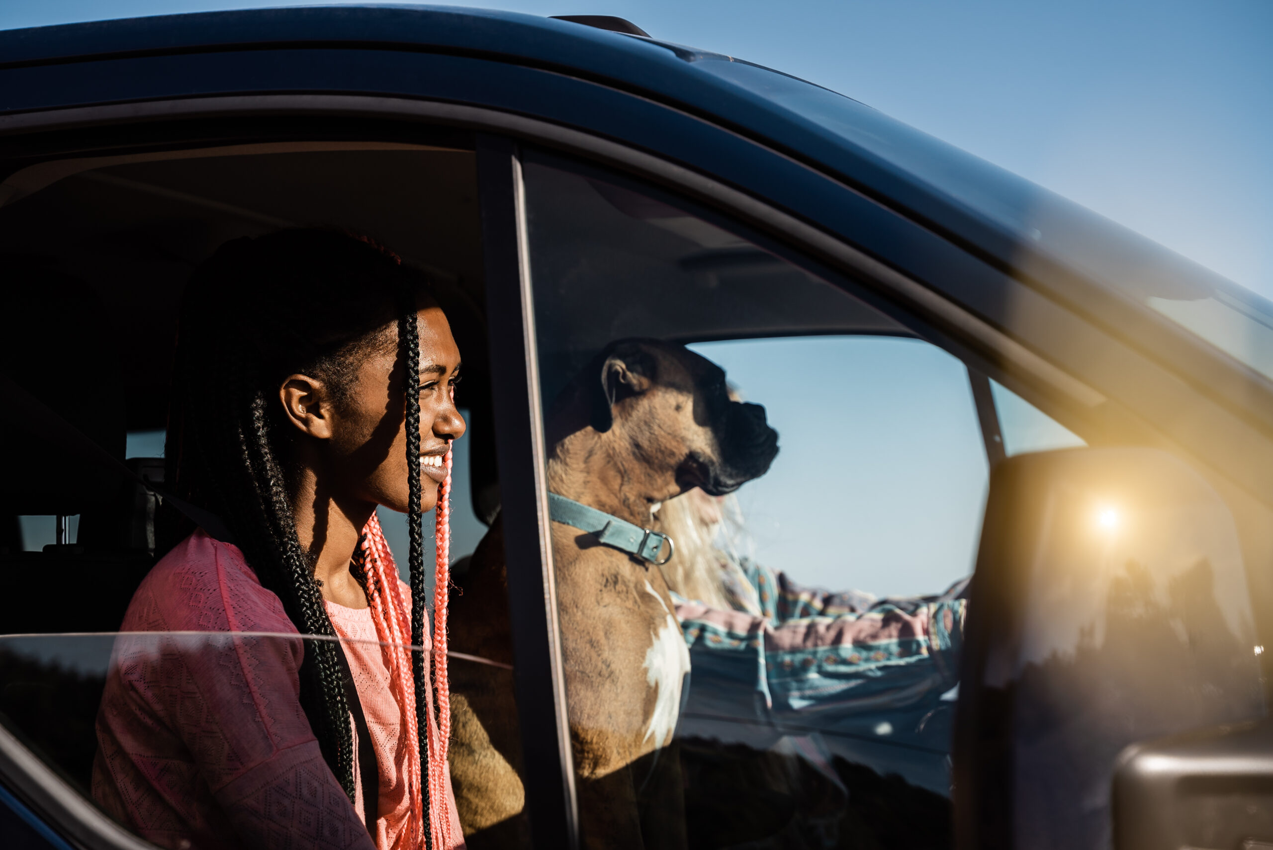 Young woman smiling in a car with a dog, enjoying a travel moment, reflecting the excitement of road trips and rental car experiences.