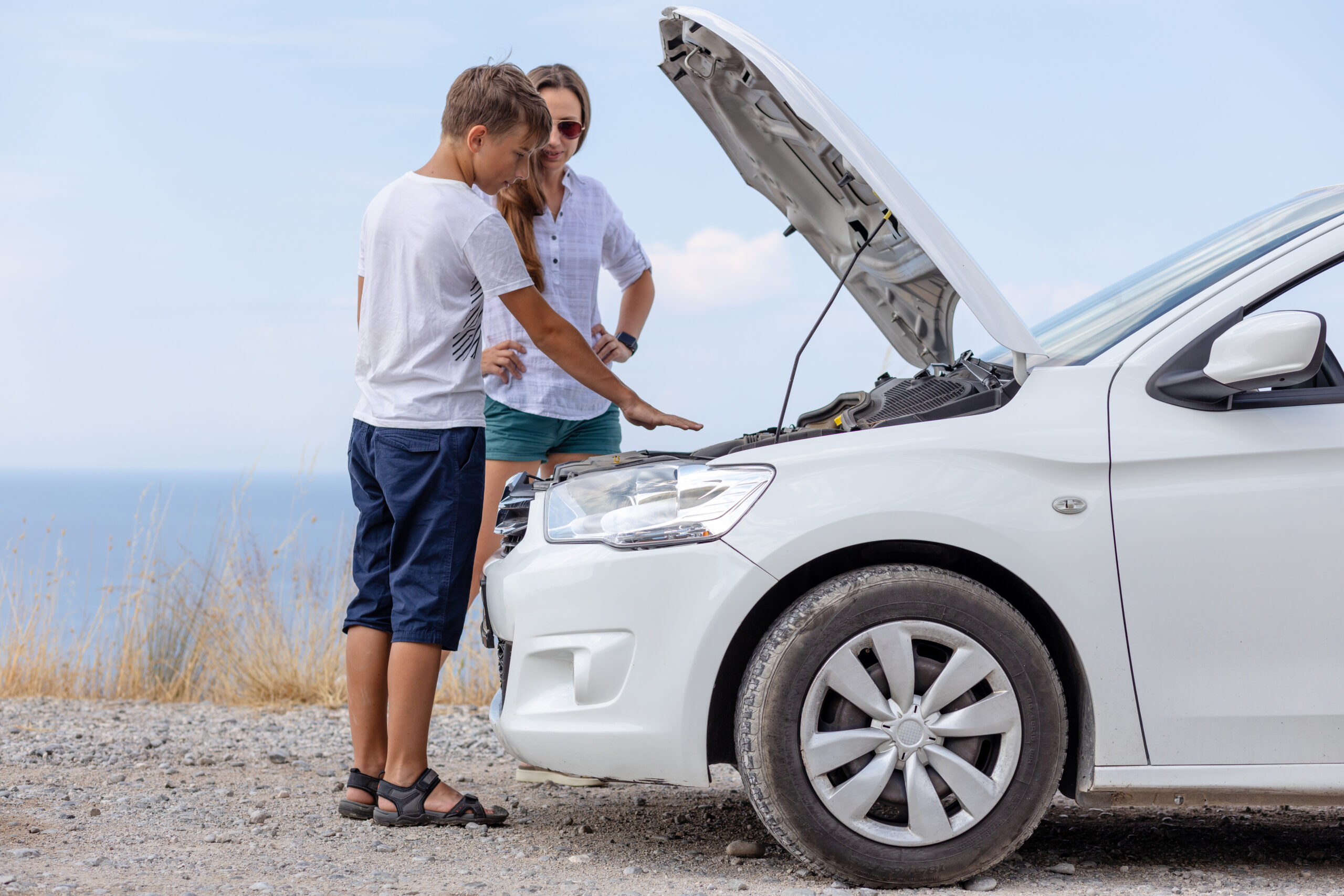 Young woman and her son inspecting the engine of a white car during a road trip, emphasizing vehicle safety checks for seniors.